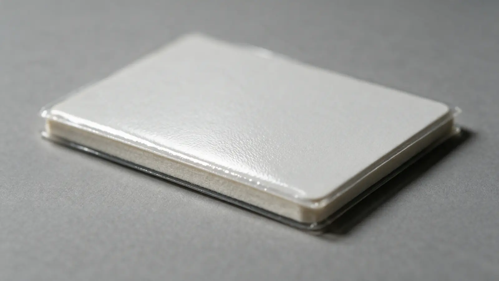 A blank white card photographed at a low angle under raking light so its surface texture and layered edge are visible.